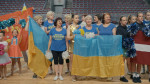 Team Ukraine keski-ikäisiä naisia sinisissä t-paidoissa valkoiset pompom pallerot käsissä ja Ukrainan liput käsissä. 